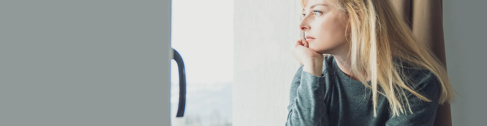 Pensive Blonde Woman sitting on windowsill looking out window. Copy space